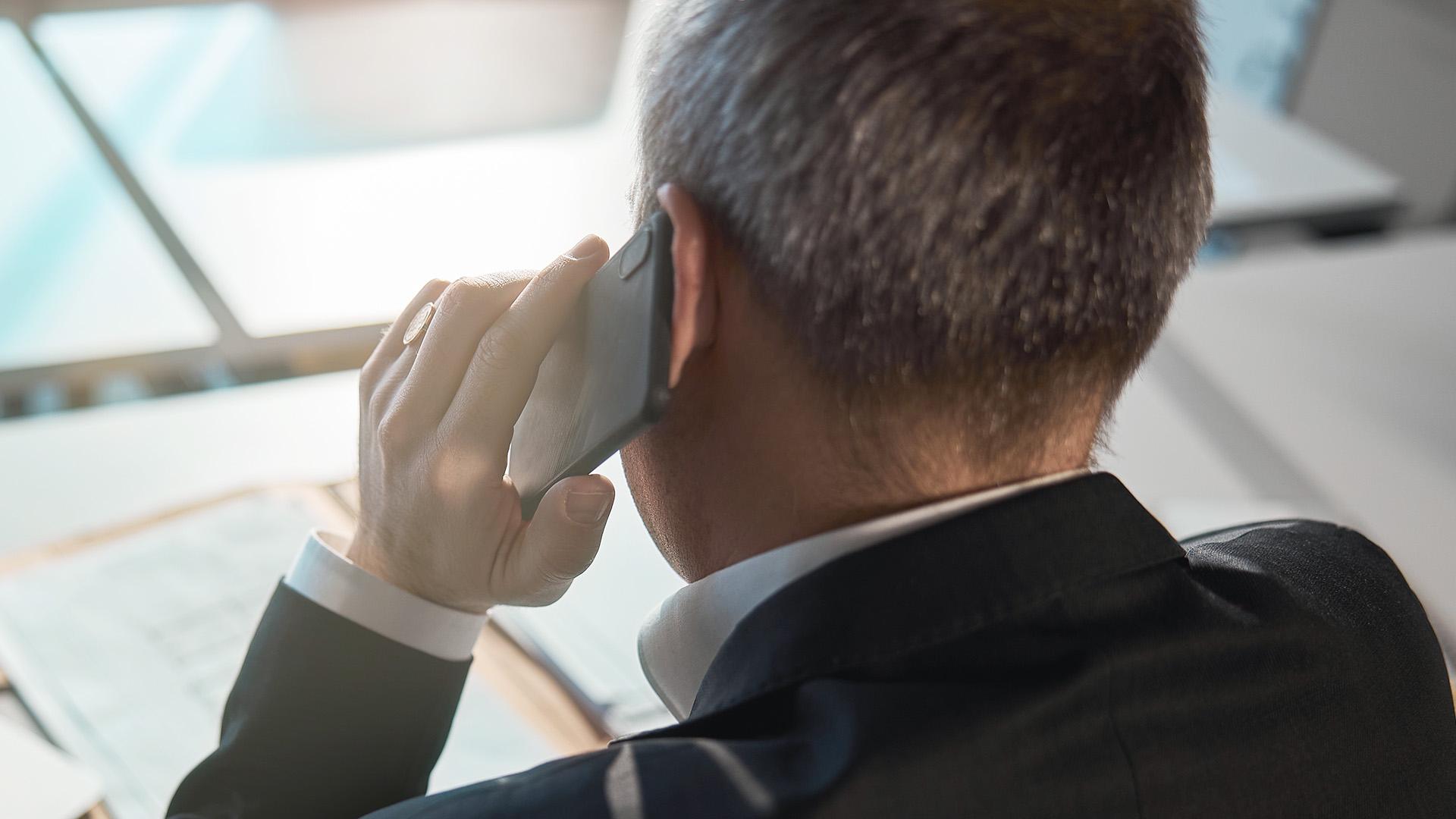 Business man in black suit on the phone, calling someone looking at desk and documents