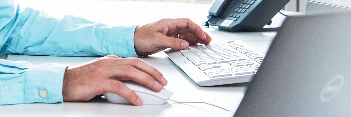 Hands of a man with a blue shirt using a mouse and and a keyboard