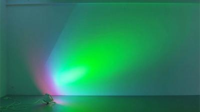 Lamp standing on floor shining onto wall, breaking the light into different colours such as purple, bright blue, but mainly vivid green